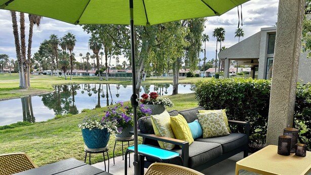 Eine Terrasse im Freien mit einem grünen Sonnenschirm, einer Couch mit Kissen, einem Tisch und Stühlen.