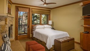 A bedroom with a bed, a wooden headboard, a stone fireplace, a balcony, and a television.
