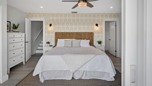 A bedroom with a large bed, a ceiling fan, a staircase, and a wall with a leaf pattern.