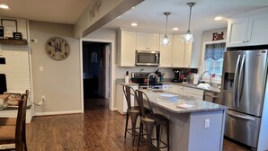 A modern kitchen with white cabinets, a stainless steel refrigerator, a built-in microwave, and a large island with bar stools. - Spacious 4 bedroom, 3 bath home with hot tub and mountain views.  (Luray)