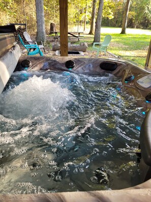 A hot tub with water jets, surrounded by outdoor seating and trees. - Spacious 4 bedroom, 3 bath home with hot tub and mountain views. (Luray)
