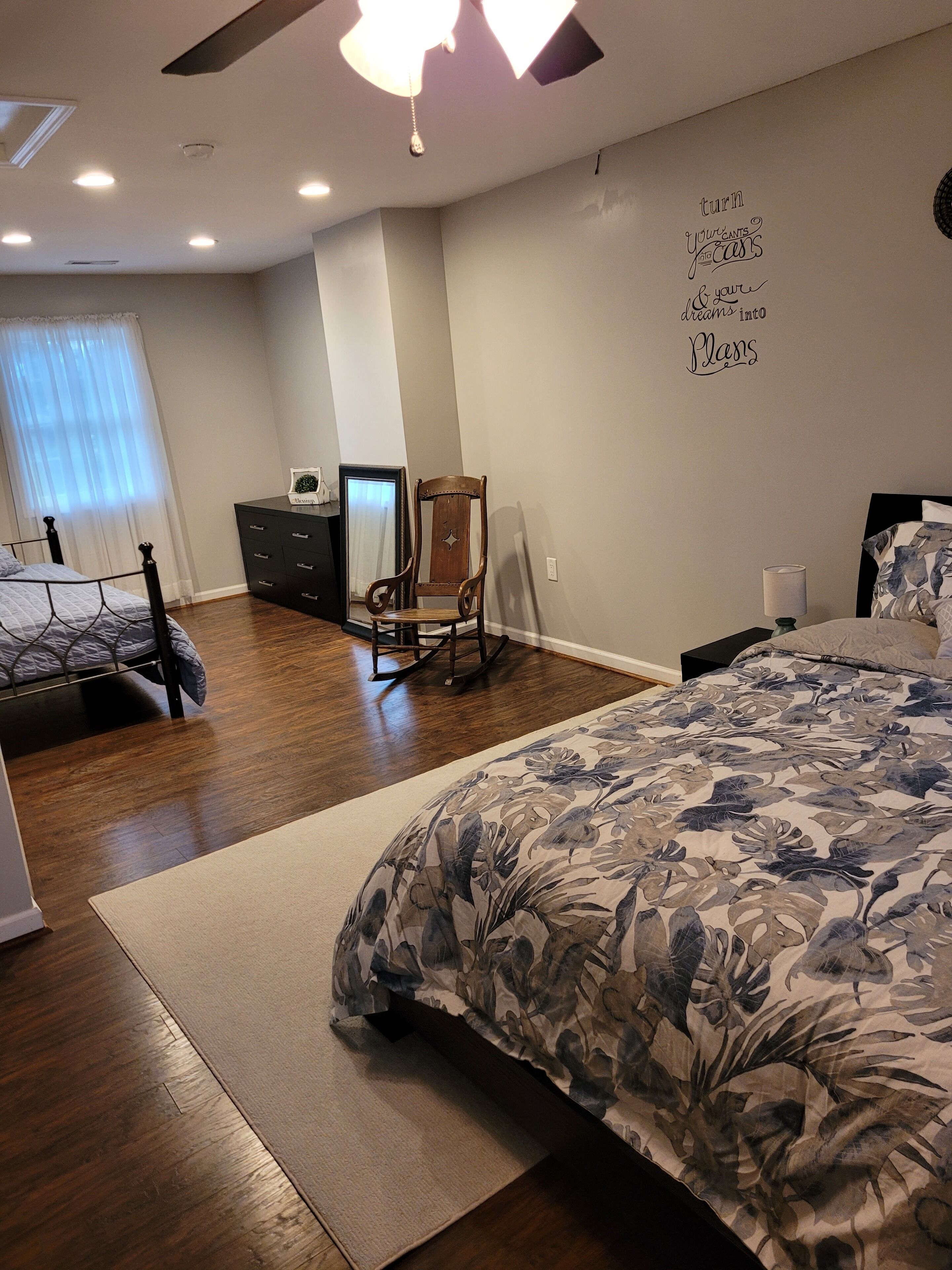 A bedroom with a large bed, a rocking chair, a dresser, and a mirror.