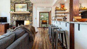 Una sala de estar moderna con chimenea de piedra, un sofá y una zona de cocina con taburetes de bar.