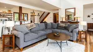 Amplia sala de estar con un sofá seccional gris, una mesa de centro de madera y una escalera que conduce a otro nivel.