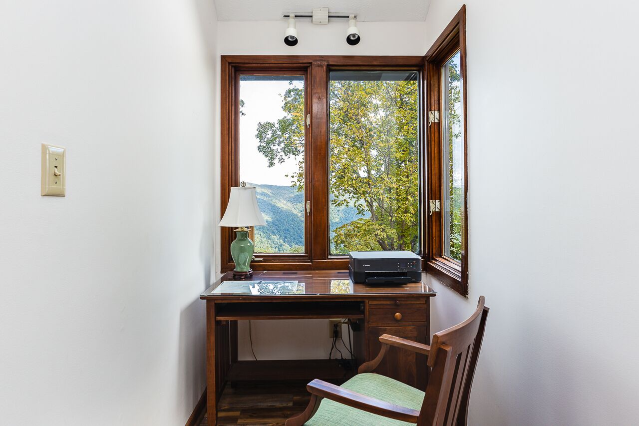 A corner desk with a lamp, a printer, and a view of a mountainous landscape through a window.
