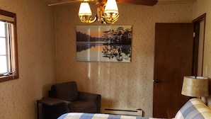 Ein Schlafzimmer mit einem Bett, einem Sessel, einem Deckenventilator, einer Wandlampe und einer Tür.