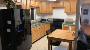 A compact kitchen with wooden cabinets, a refrigerator, a microwave, an oven, and a dining table with chairs.
