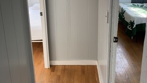 A room with a wooden floor, a bed with a white bedspread, and a window with a view of greenery.