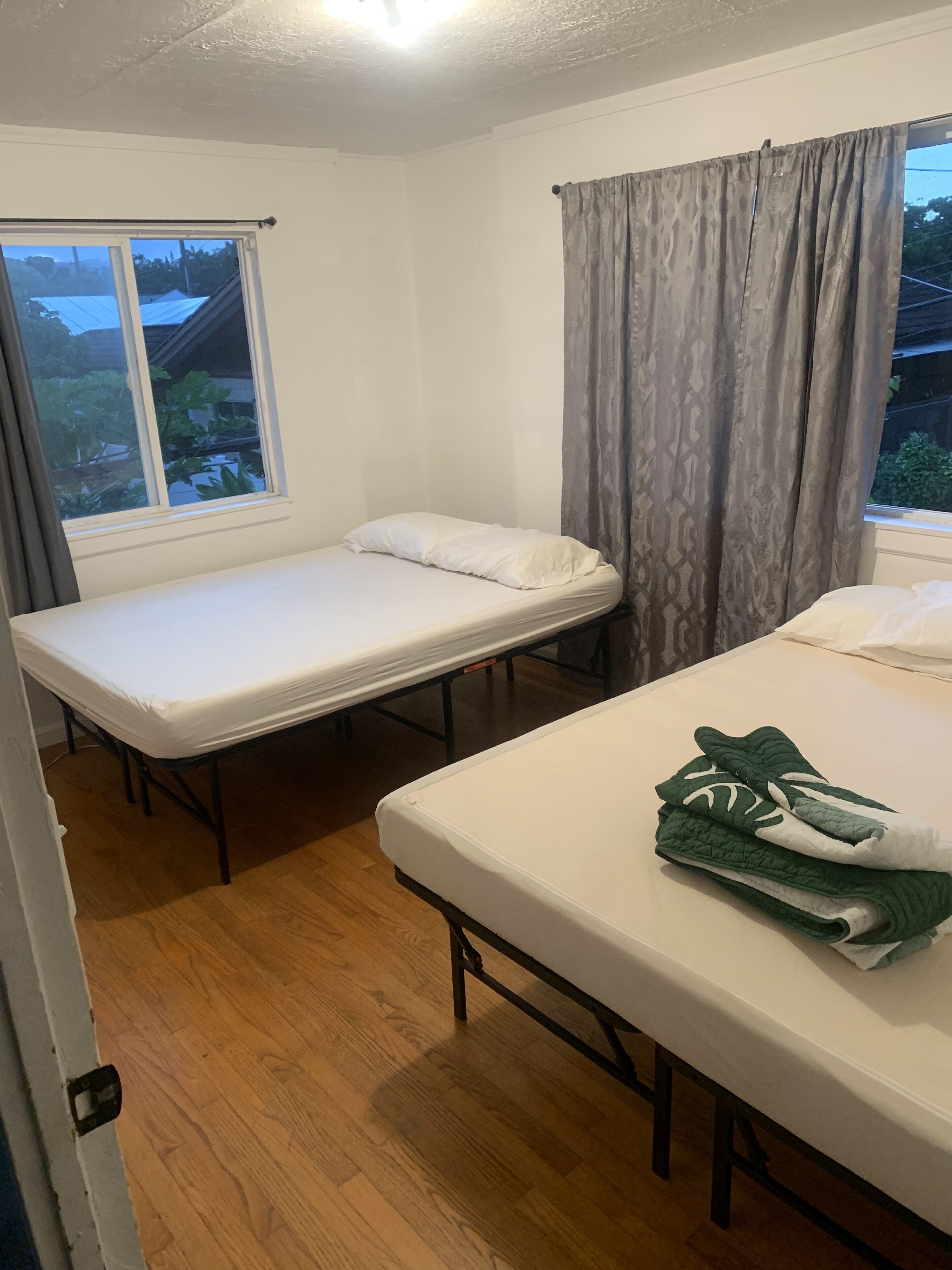 A room with two single beds, a window with curtains, and a view of greenery outside.
