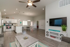 A spacious living area with a dining table, kitchen, and a flat-screen TV mounted on the wall.