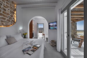 Ein modernes Hotelzimmer mit einem großen Bett, einer Steinwand, einem Balkon mit Aussicht und einem an der Wand befestigten Fernseher.