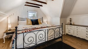 Een slaapkamer met een schuine kap, een bed met een bedsprei met een patroon, een nachtkastje met een lamp en een kledingkast met lades.