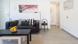 A modern living room with a black sofa, a small table with fruit, a floor lamp, and a painting of a tree. - Sunny Angels by Canariasgetaway (Mogán)