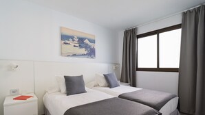 A hotel room with two beds, a nightstand, a window with curtains, and a wall-mounted painting. - Sunny Angels by Canariasgetaway (Mogán)