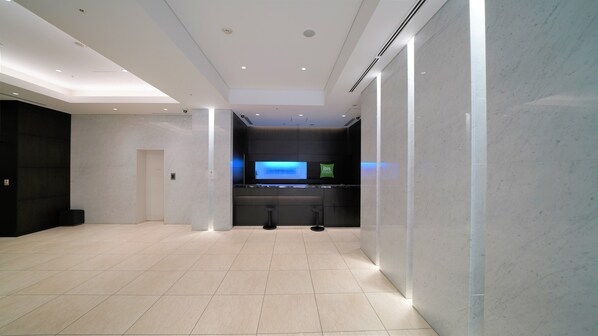 A modern hotel lobby with a reception desk, seating area, and a large digital display.
