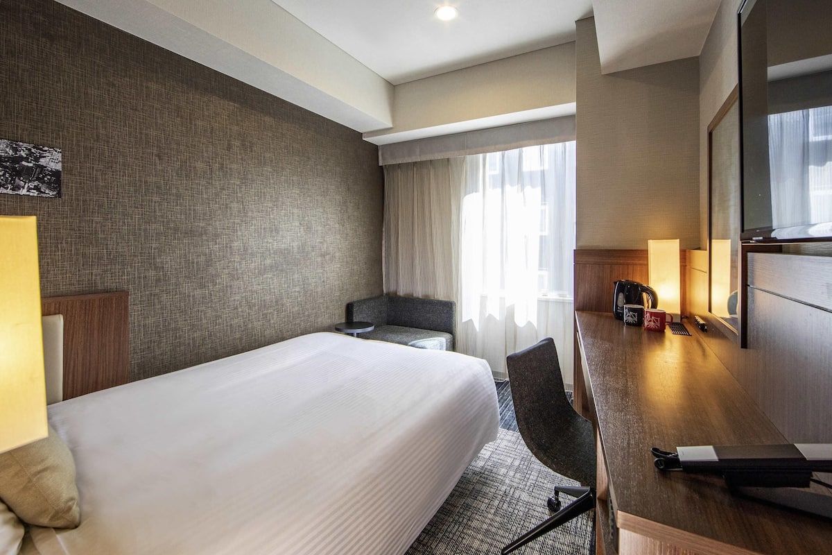 A hotel room with a large bed, a desk with a chair, a coffee maker, and a mirror.