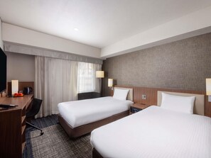 Habitación de hotel con dos camas, un escritorio, una silla, un televisor y una ventana con cortinas.