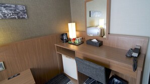 Habitación de hotel con escritorio de madera, espejo, lámpara, cafetera, refrigerador pequeño y teléfono.
