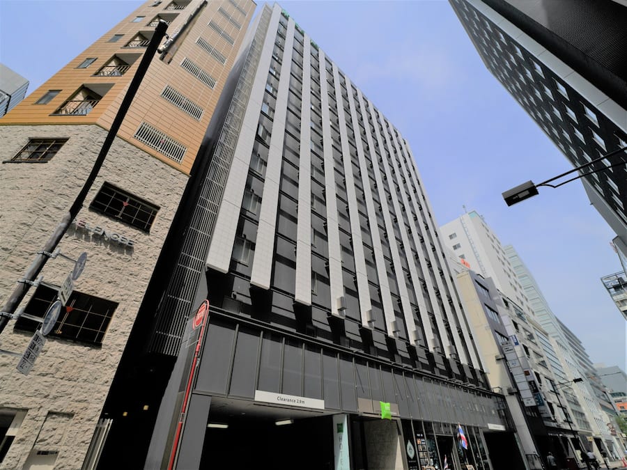 Un edificio de gran altura con un diseño arquitectónico moderno, que presenta una entrada destacada con un cartel que indica una altura libre de 2,9 metros.