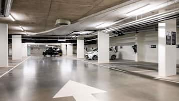 Garagem de estacionamento com pilares brancos, setas indicativas no chão e estações de carregamento para veículos elétricos.