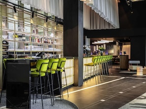 A bar area with a long counter, green bar stools, and shelves stocked with bottles and glasses. - TRIBE Amsterdam City (Amsterdam)