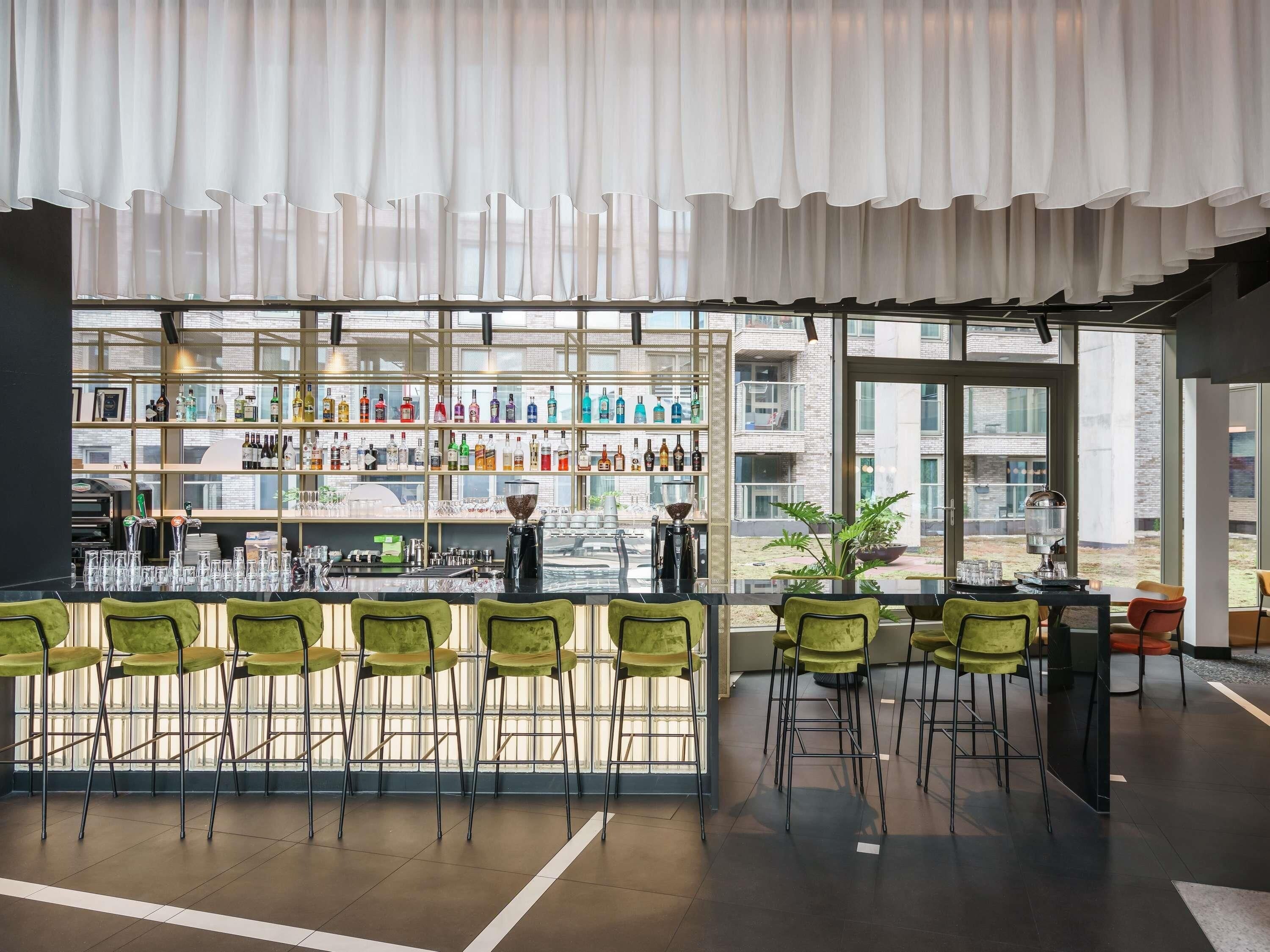 Een barruimte met een modern design, met een bar, krukken en een groot raam met uitzicht op buiten.