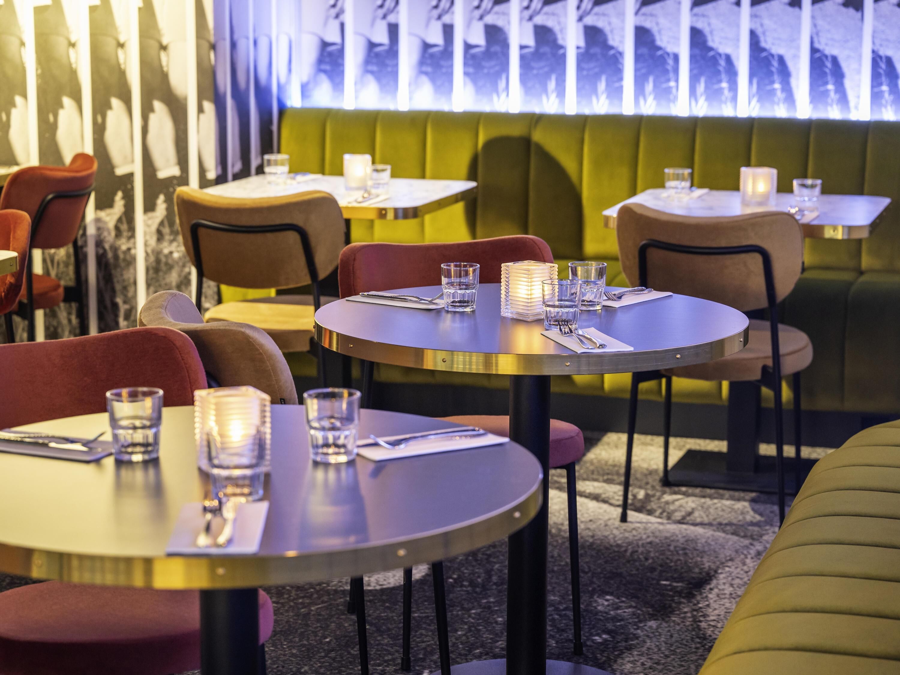A restaurant interior with round tables, chairs, and a green cushioned bench.