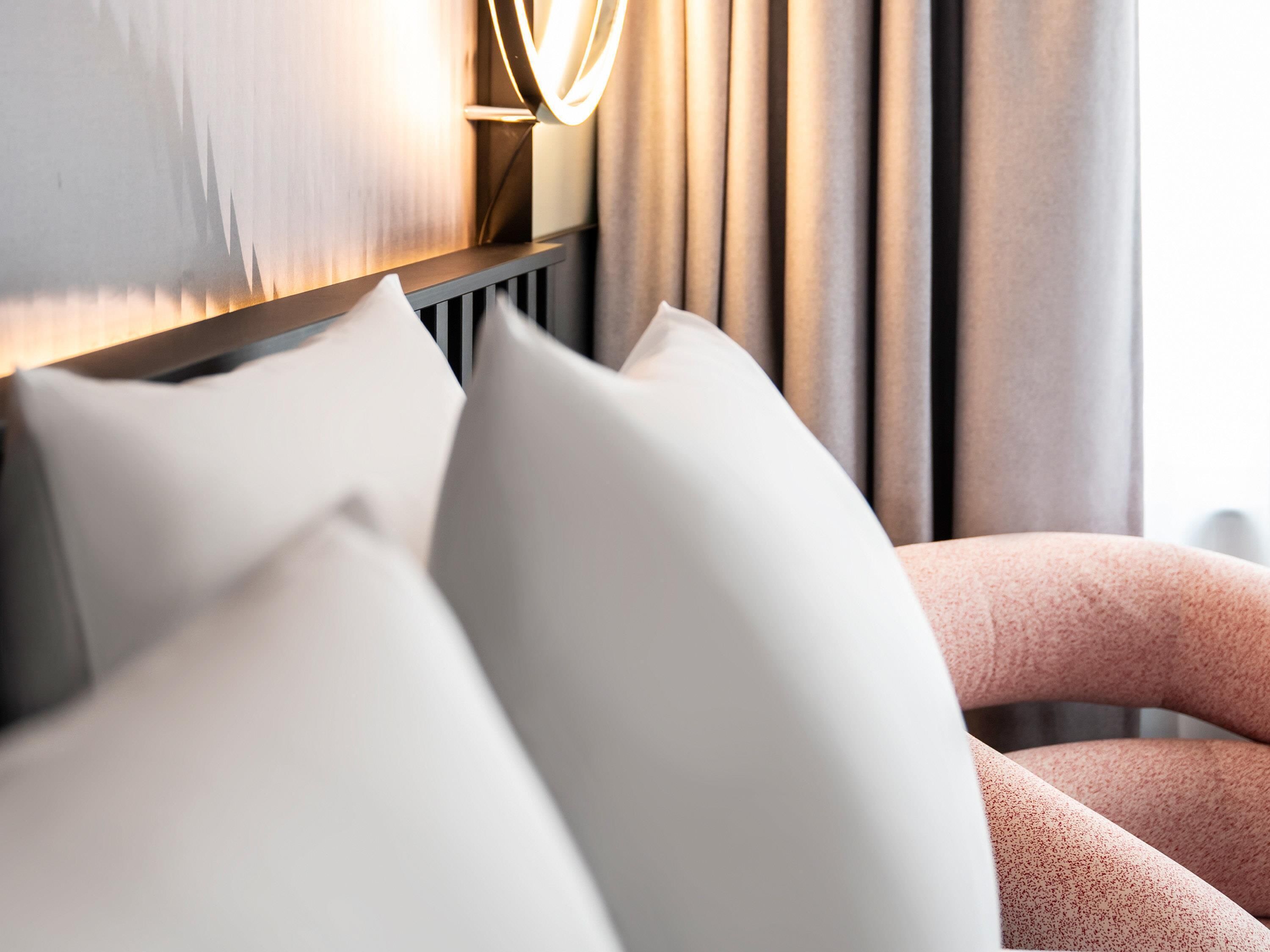 Een moderne hotelkamer met een groot bed, witte kussens en een hoofdeinde met een lamp.