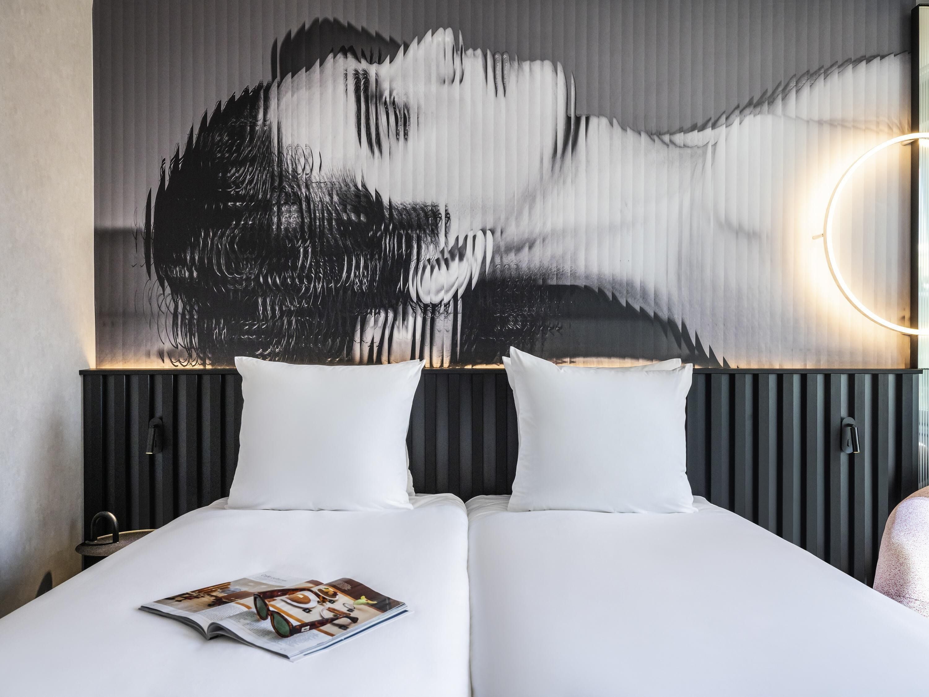 A double bed with white bedding, a magazine on the bed, and a large abstract painting on the wall.