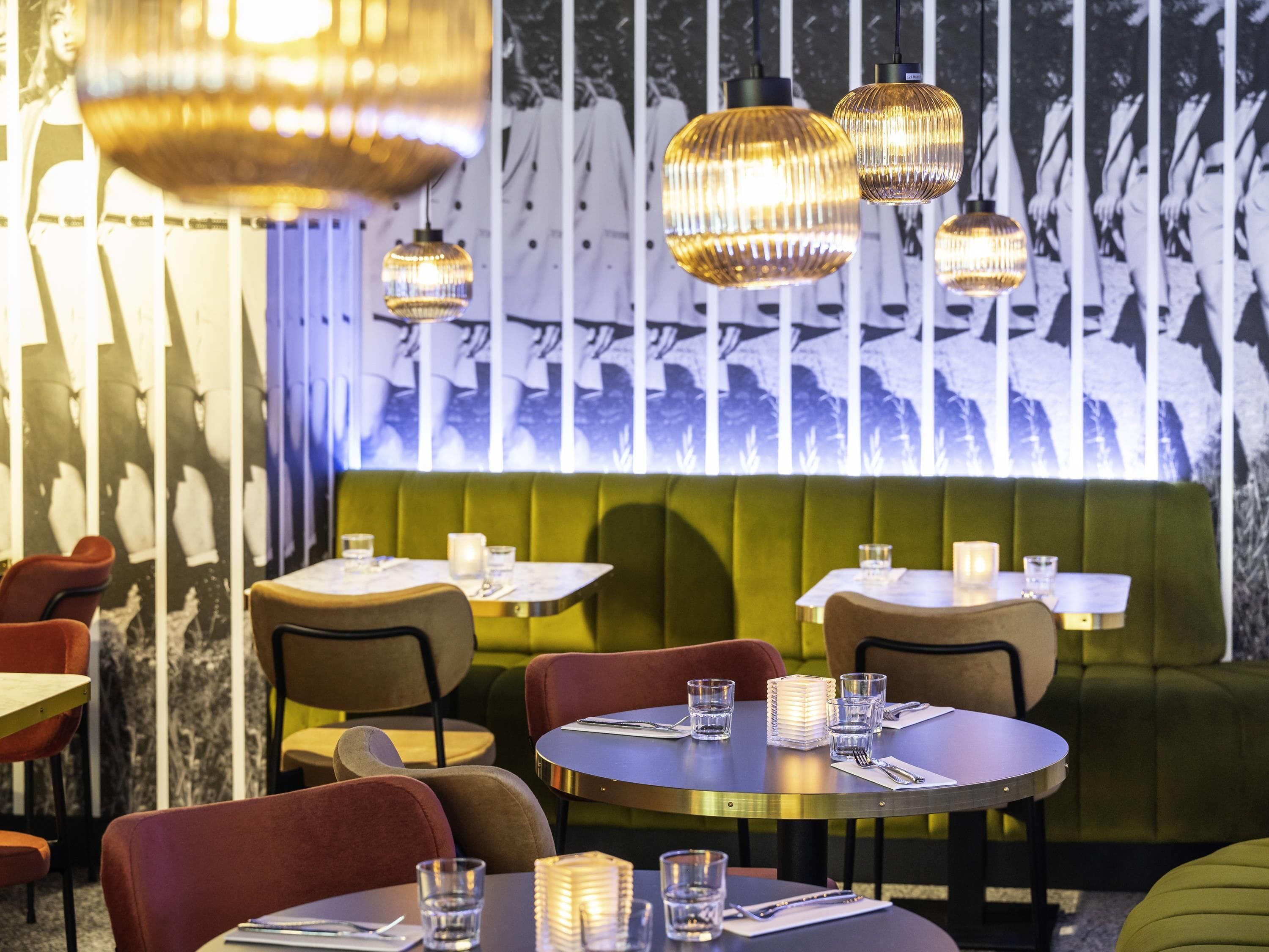 L'intérieur d'un restaurant avec des tables rondes, des banquettes confortables et des luminaires suspendus.