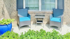 A patio area with two wicker chairs with blue cushions, a small table, and a large potted plant. - Quiet 4 bedroom villa with tons of space (Murfreesboro)