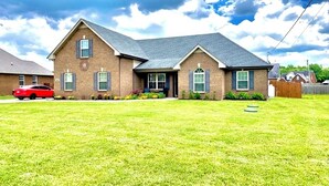 A two-story house with a brick exterior, a front porch, and a red car parked in the driveway. - Quiet 4 bedroom villa with tons of space (Murfreesboro)