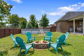 A backyard with a fire pit, four chairs, a ladder, and a barbecue grill.