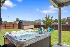 Een achtertuin met een jacuzzi, een houten terras en tuinmeubilair.