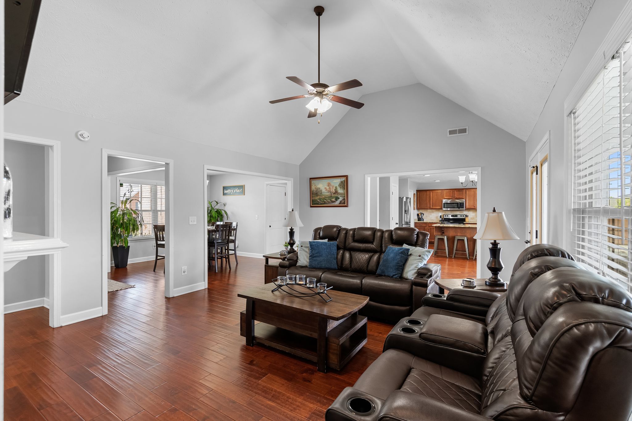 A spacious living room with a ceiling fan, a dining area with a table and chairs, and a kitchen in the background.