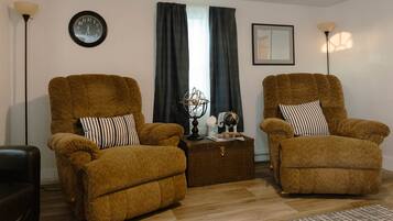 A living room with two brown armchairs, a small side table with a globe and books, a wall clock, and a framed picture.