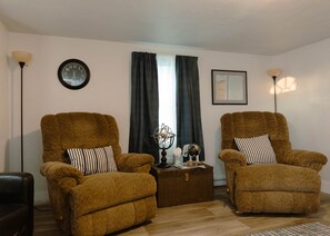 A living room with two brown armchairs, a small side table with a globe and books, a wall clock, and a framed picture. - Walleye Waters – 2BR Mobridge Stay (Mobridge)