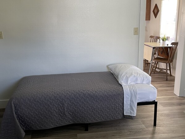 Een enkel bed met een grijze deken en wit kussen in een kamer met houten vloer en witte wanden.