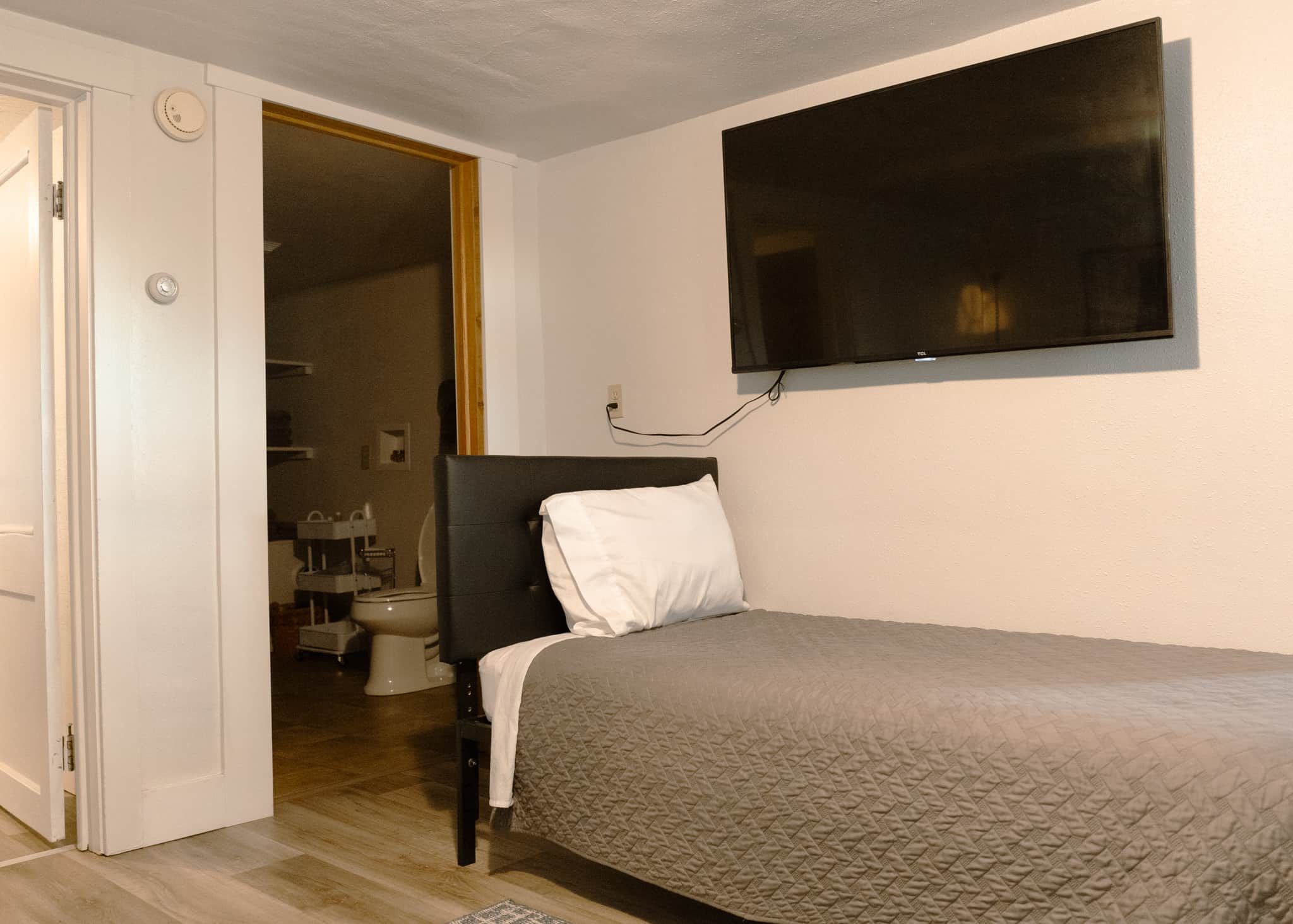 A bedroom with a bed, a television mounted on the wall, and a door leading to a bathroom.