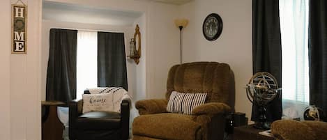 Un salón con un sillón marrón, una mesita, un globo terráqueo y un reloj en la pared.