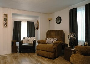 A living room with a brown armchair, a small table, a globe, and a clock on the wall.