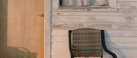 A wooden door with a window above it, a wicker chair in front, and a wooden deck.