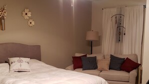 Une chambre à coucher avec un lit, un canapé, un ventilateur de plafond et une fenêtre avec des rideaux.