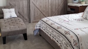 Un dormitorio con cama, una banca, una mesita de noche, una lámpara y un ventilador de techo.