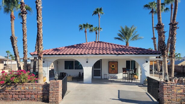Une maison de plain-pied avec un toit recouvert de tuiles rouges, une entrée en briques et un petit patio aménagé avec du mobilier d’extérieur.