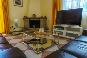 Uma sala de estar com uma mesa de centro de vidro, sofás de couro, uma lareira e uma televisão.