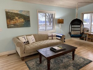 A living room with a beige sofa, a wooden coffee table, a hanging chair, and a painting on the wall.