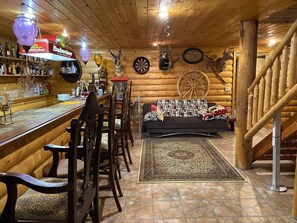 A cozy log cabin interior with a bar area, wooden walls, and rustic decor including antlers and a spinning wheel. - My house is unique,  welcome EVERYONE to  enjoy beautiful VALLEY in Swane Lake.  (Swan Lake)