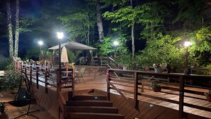 Una terraza de madera con una escalera que lleva a una zona cubierta, rodeada de follaje.
