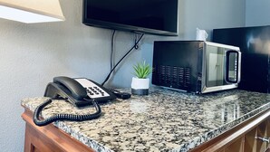 A kitchen with a granite countertop, a microwave, a telephone, and a small potted plant. - Extended Stay SA (San Antonio)